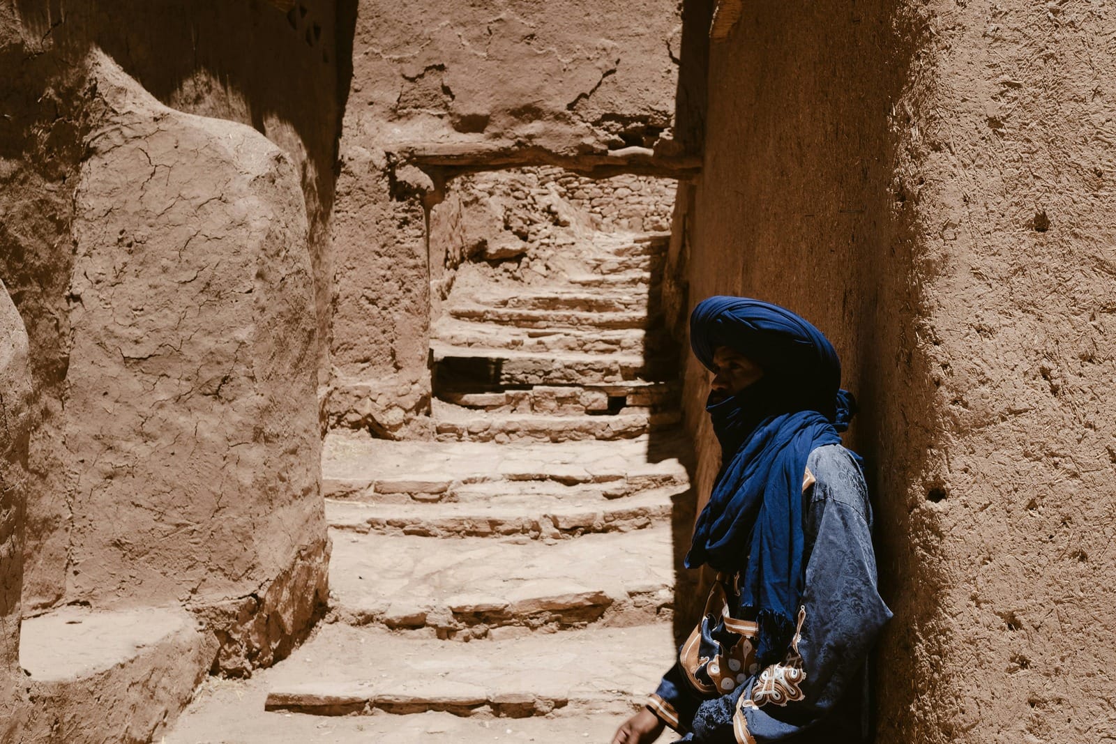 Berber man in blue turban resting by stone steps inside Ait Benhaddou