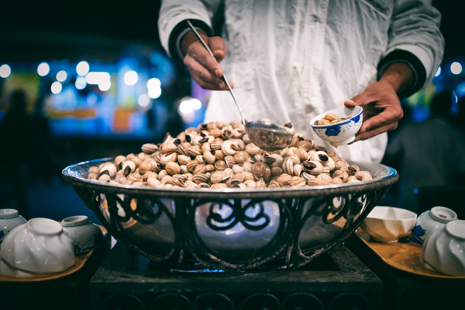 Vendor ladling snail soup from a huge bowl into porcelain cups