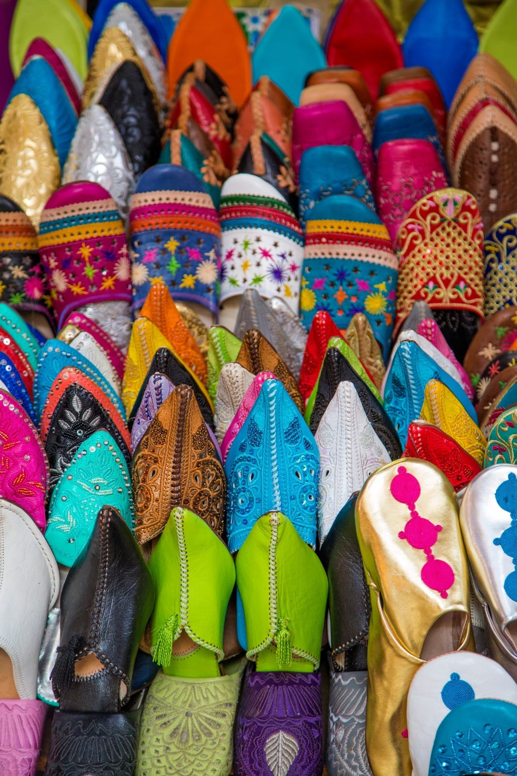 Rows of embroidered leather babouche slippers stacked at a Marrakech souk stall