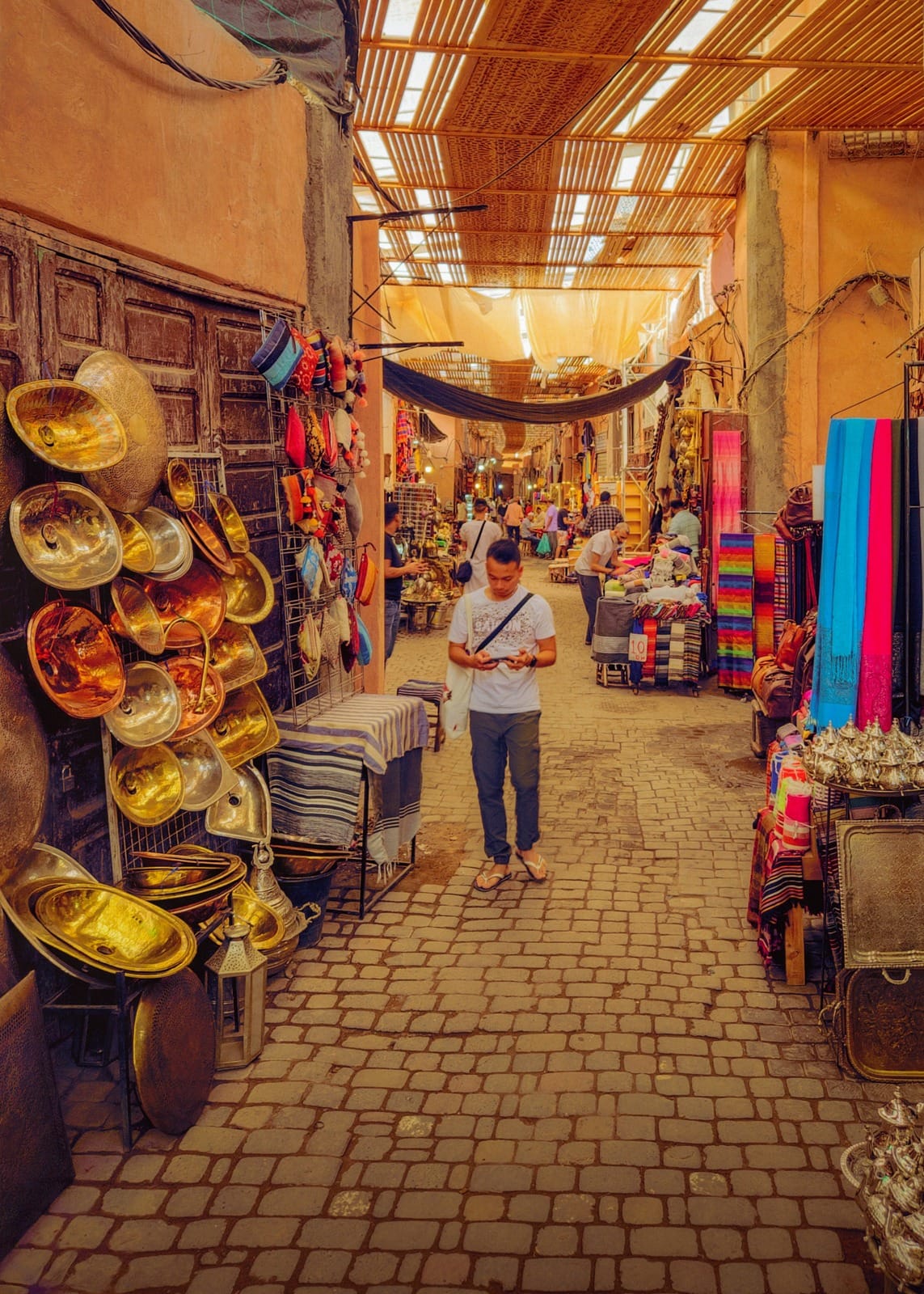 Copper and brass basins beside a shopper in a covered souk alley